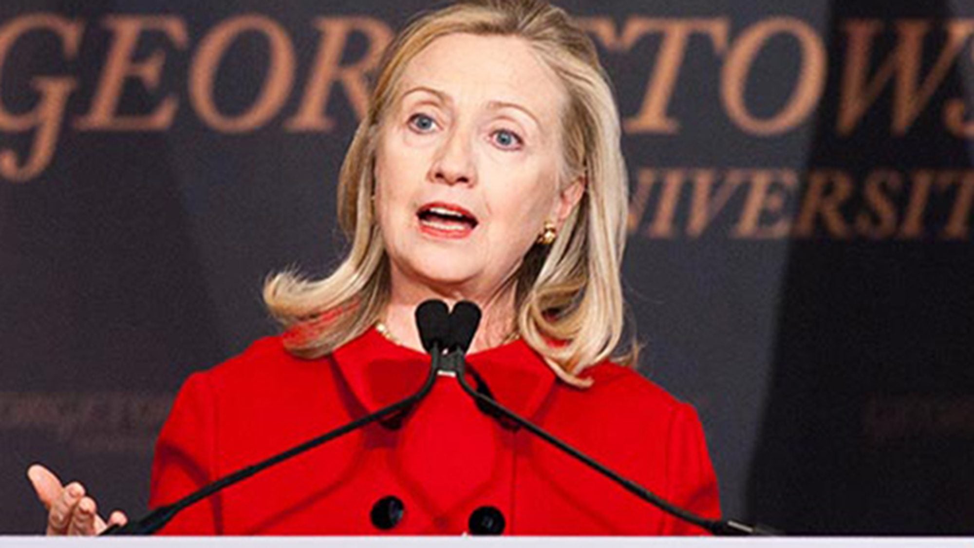 Hillary Rodham Clinton speaking into a microphone at podium with Georgetown University banner behind her