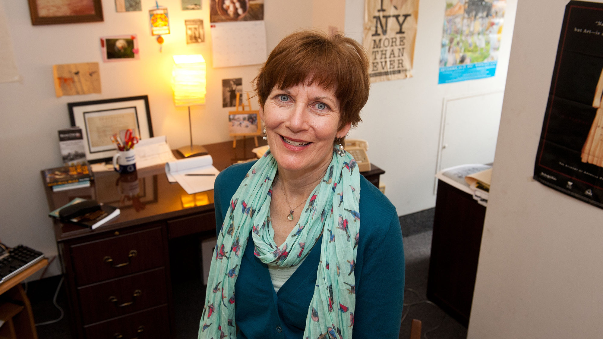 Maureen Corrigan sits in front of her desk with posters on the wall