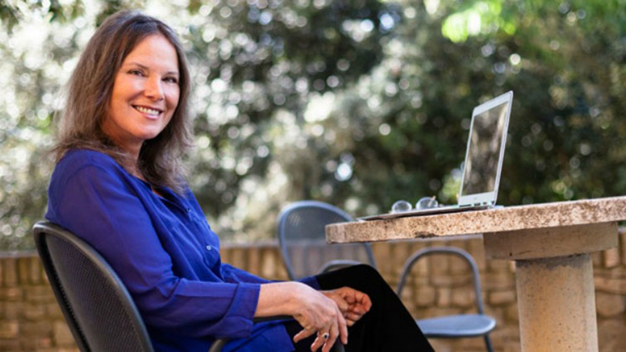 Carolyn Forché sits outside looking into the camera.