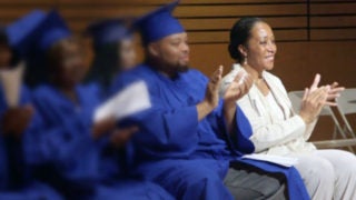 Lecester Johnson sitting and clapping next to students in caps and gowns also clapping