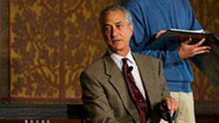 David Strathairn acting as Jan Karski on stage sitting on a bench with student actor behind him
