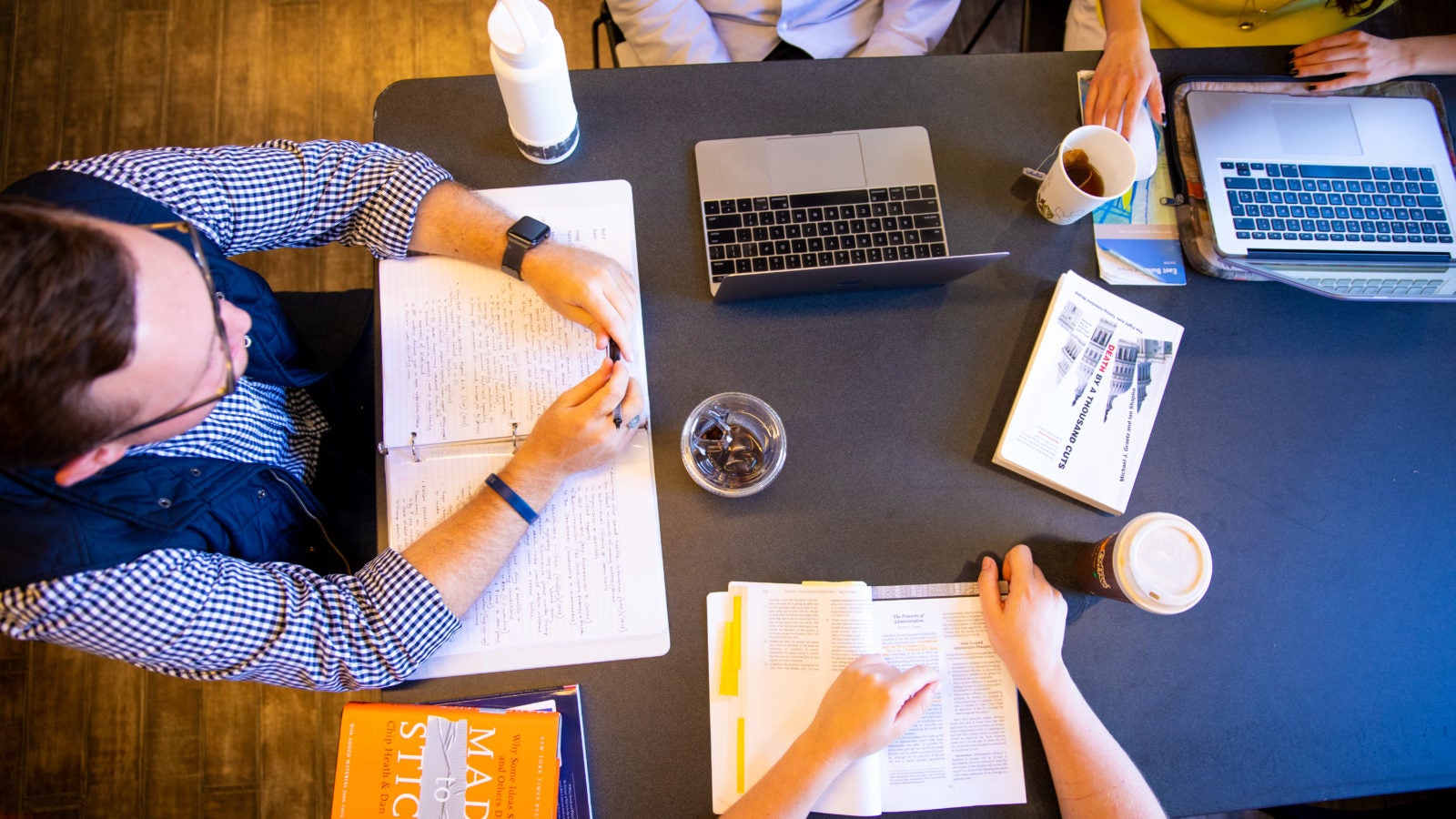 Students are gathered around a table with books and laptops open.