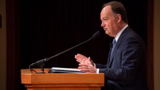 John J. DeGioia tands talking at a lectern on stage.