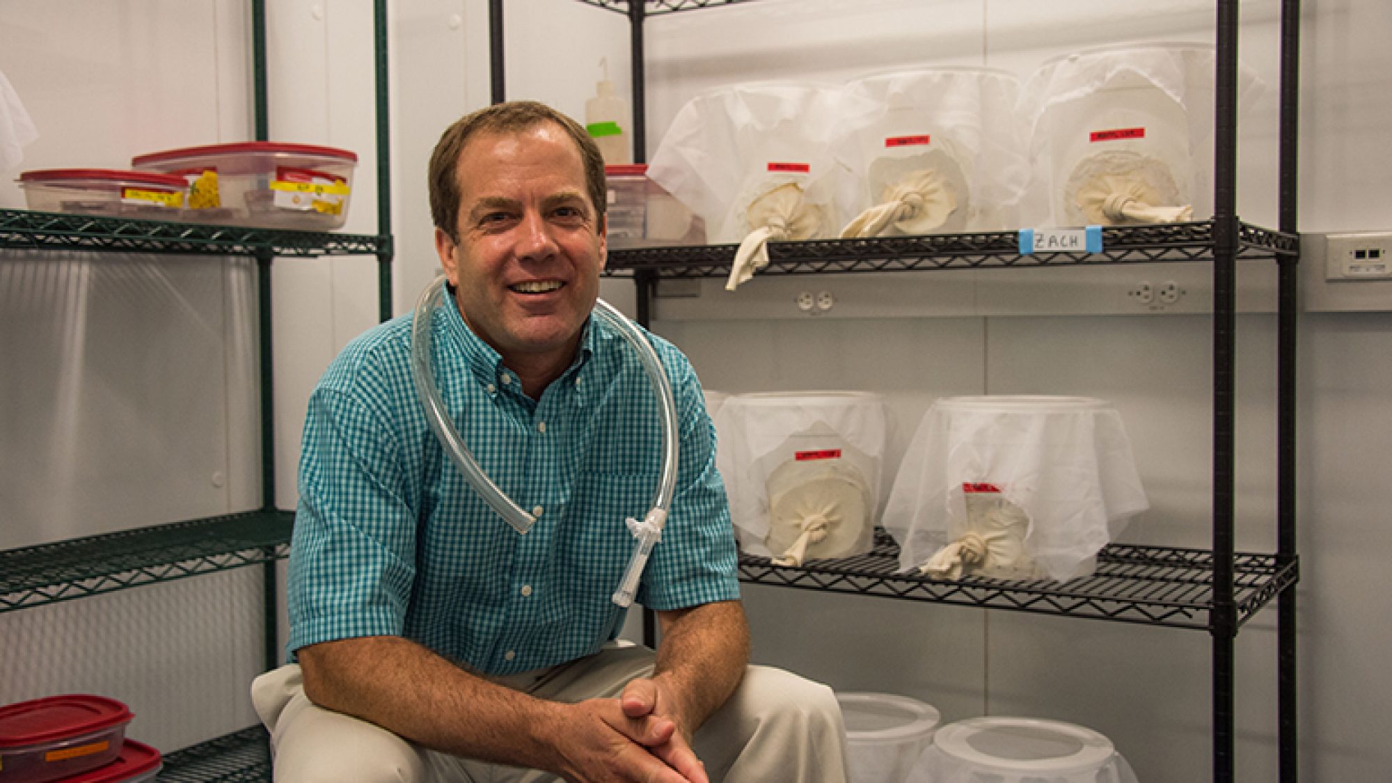 Peter Armbruster sits in his lab with covered buckets of mosquitoes