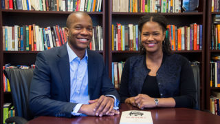 Robert Patterson and Soyica Colbert sit at a table with their book and a bookcase behind them.