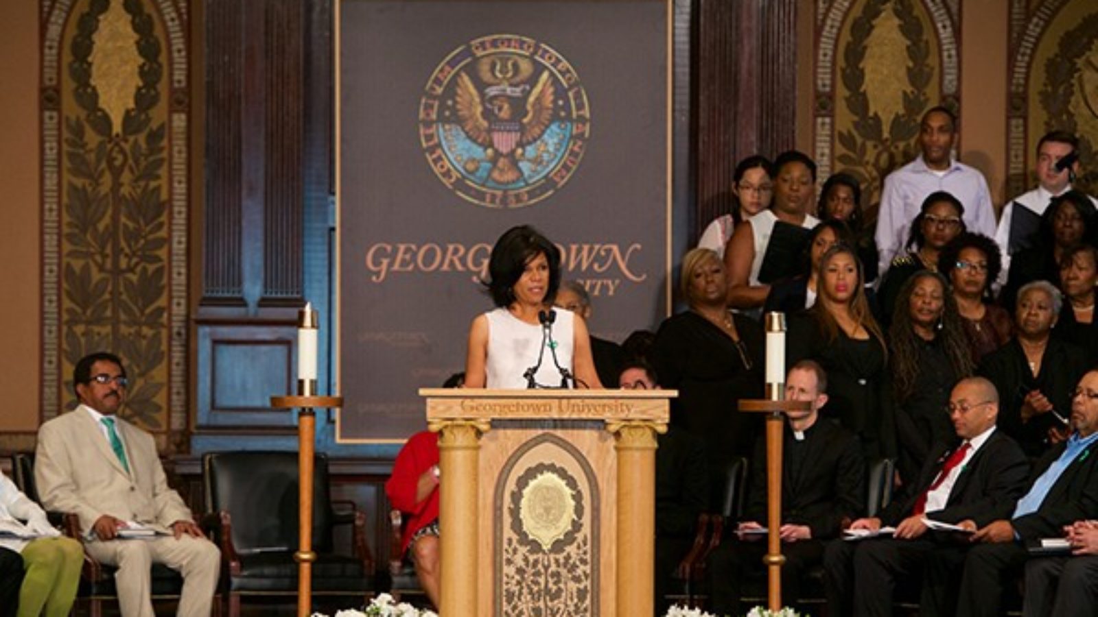 Sandra Green Thomas at the podium in Gaston Hall with a group of people standing at left