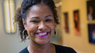 Soyica Diggs Colbert smiles into the camera with a wall of theater photos in the background to her right