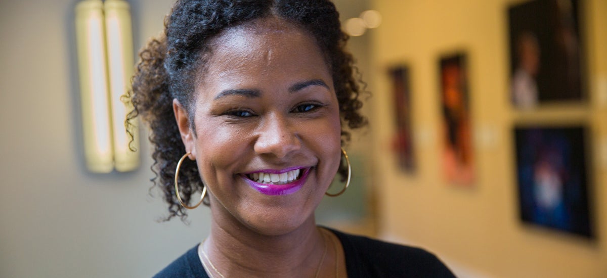 Soyica Diggs Colbert smiles into the camera with a wall of theater photos in the background to her right