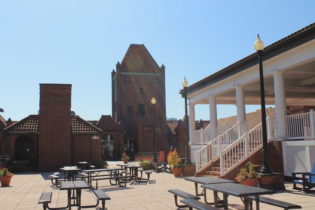 A patio on a sunny day with picnic tables and a building behind it.