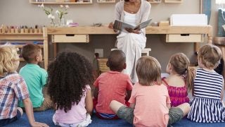 Teacher reading to a group of young children sitting on the floor.