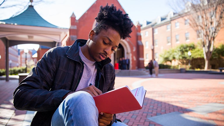 Emmanuel Thomas reading a book outside.