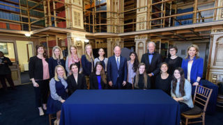 Bill McDonough and John J. DeGioia stand around a table with students and administrators
