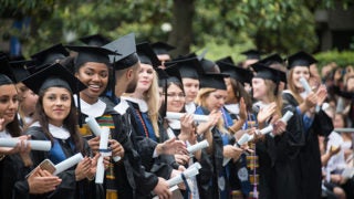 Students in cap and gowns holding diplomas