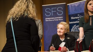 Madeleine Albright signs a book while a student looks on