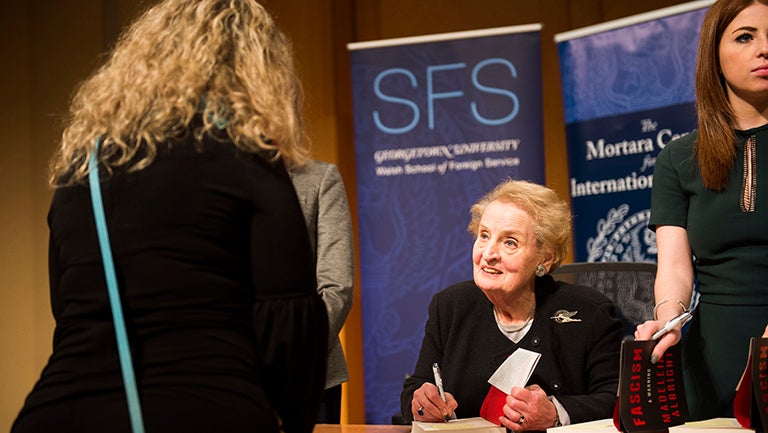 Madeleine Albright signs a book while a student looks on