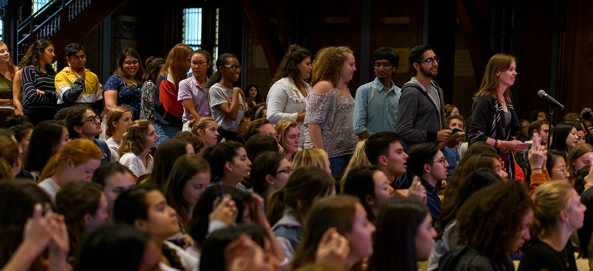 Students line up for the microphone in the aisle among a crowded audience.