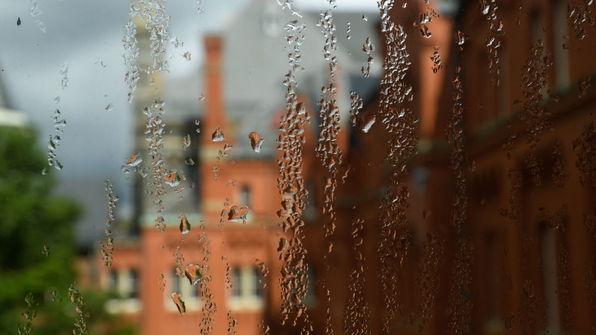 Rain trickles down a window with campus in the background