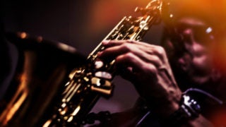 A man wearing sunglasses plays a saxaphone.