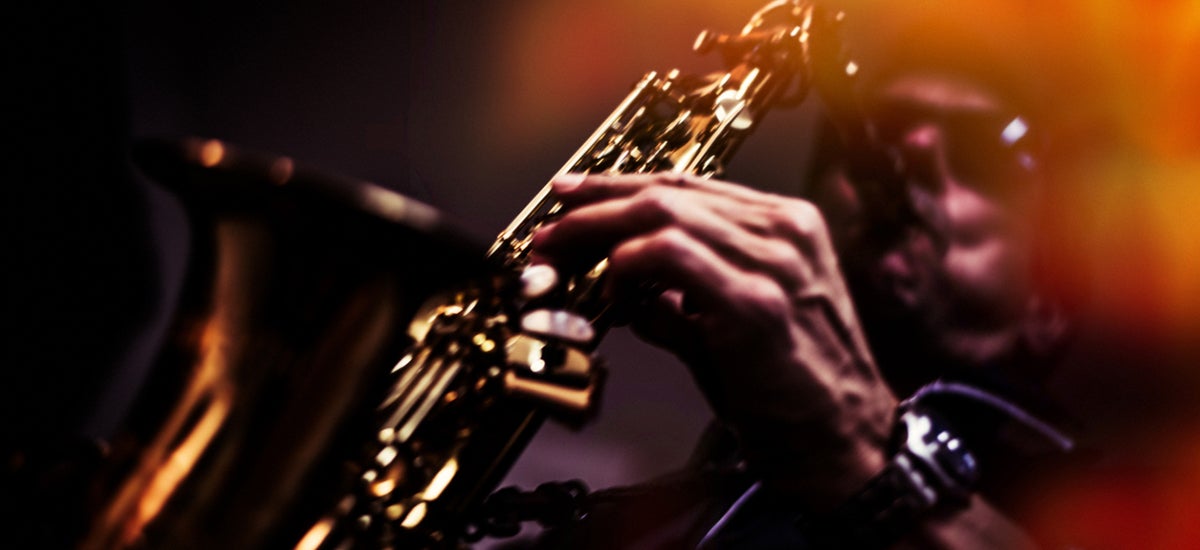 A man wearing sunglasses plays a saxaphone.