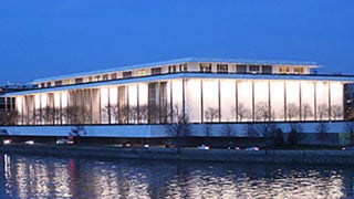 The Kennedy Centerr for the Performing Arts sits lit up at night with the Potomac River in the foreground.