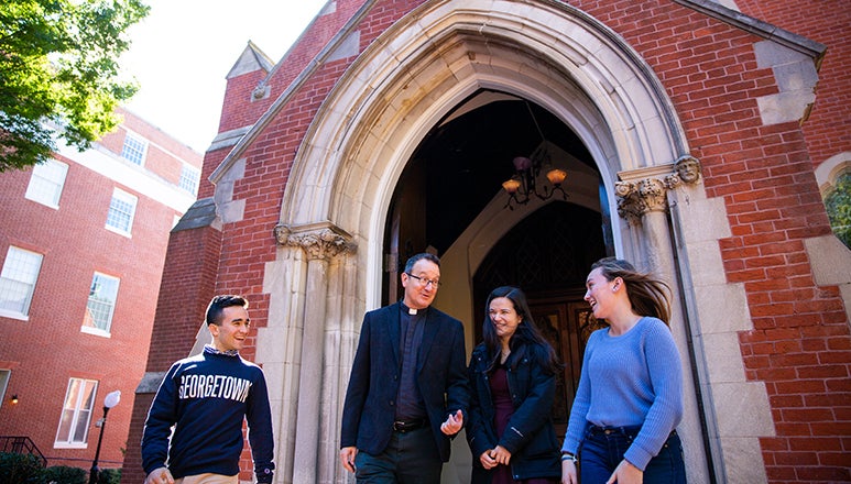 Rev. Mark Bosco, S.J. chats with students outside of Dahlgren Chapel.