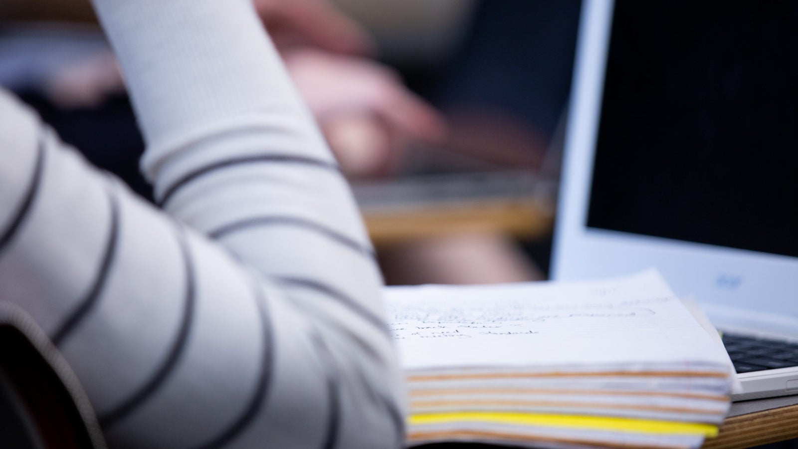 An arm and a notebook resting on a desk.