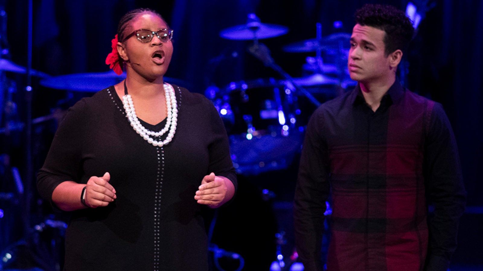 Minnie Quartey speaks to the audience during a performance as Ricardo Flores looks on.