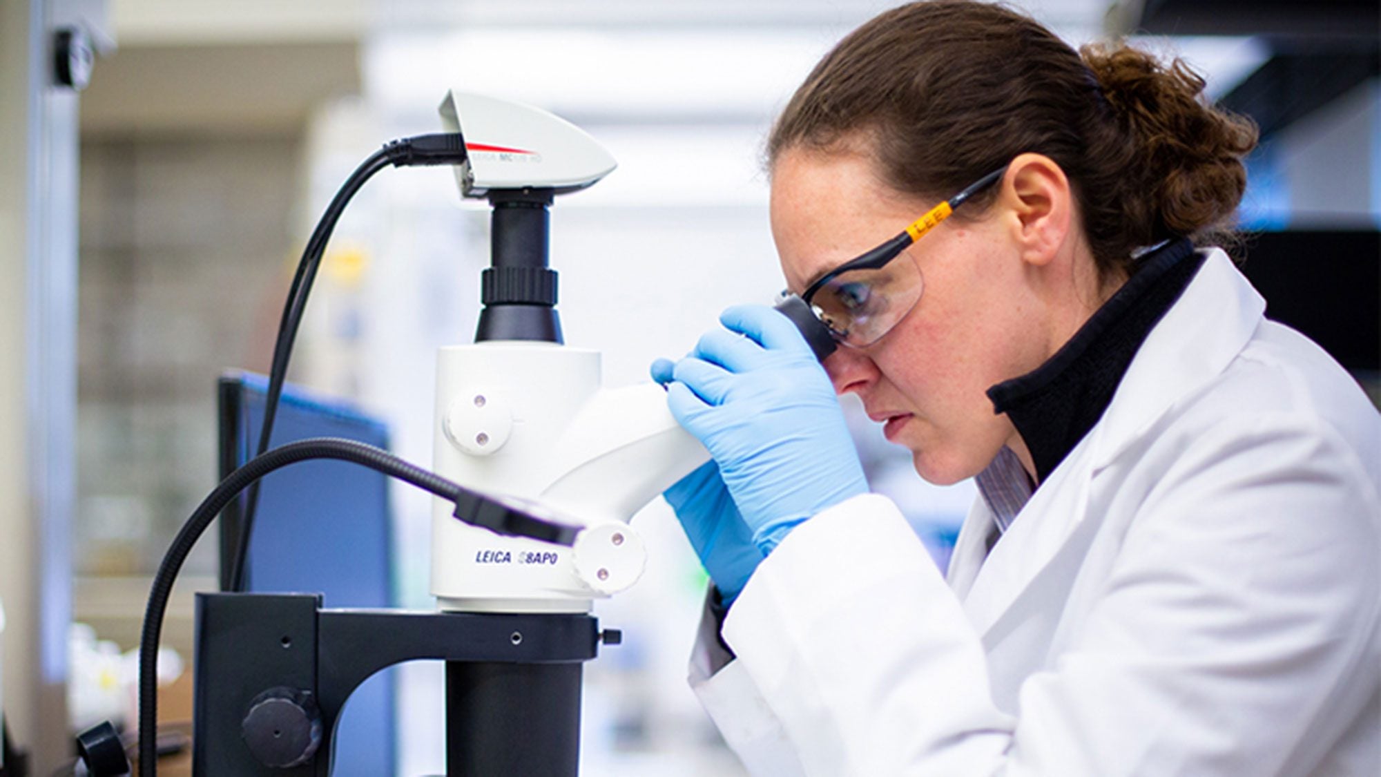 Karah Knope looks through a microscope while wearing a lab coat.