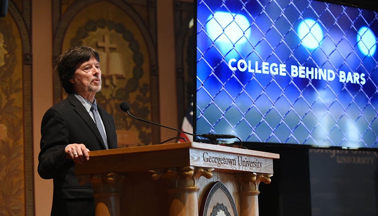 Ken Burns at podium with screen behind him reading College Behind Bars