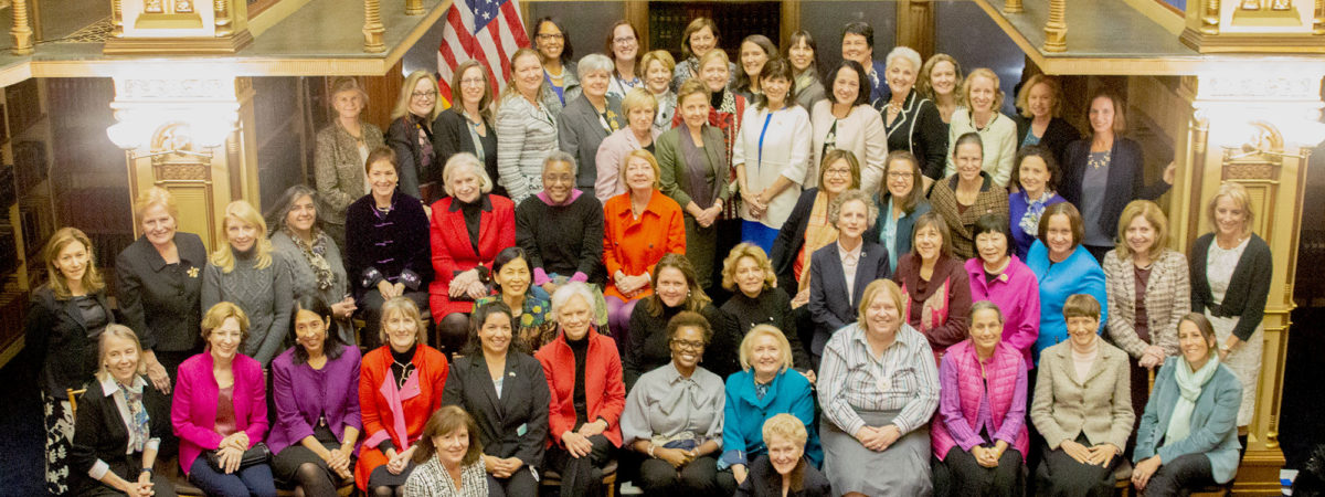 A group of about 60 women sit and stand for a photo together in Riggs Library.