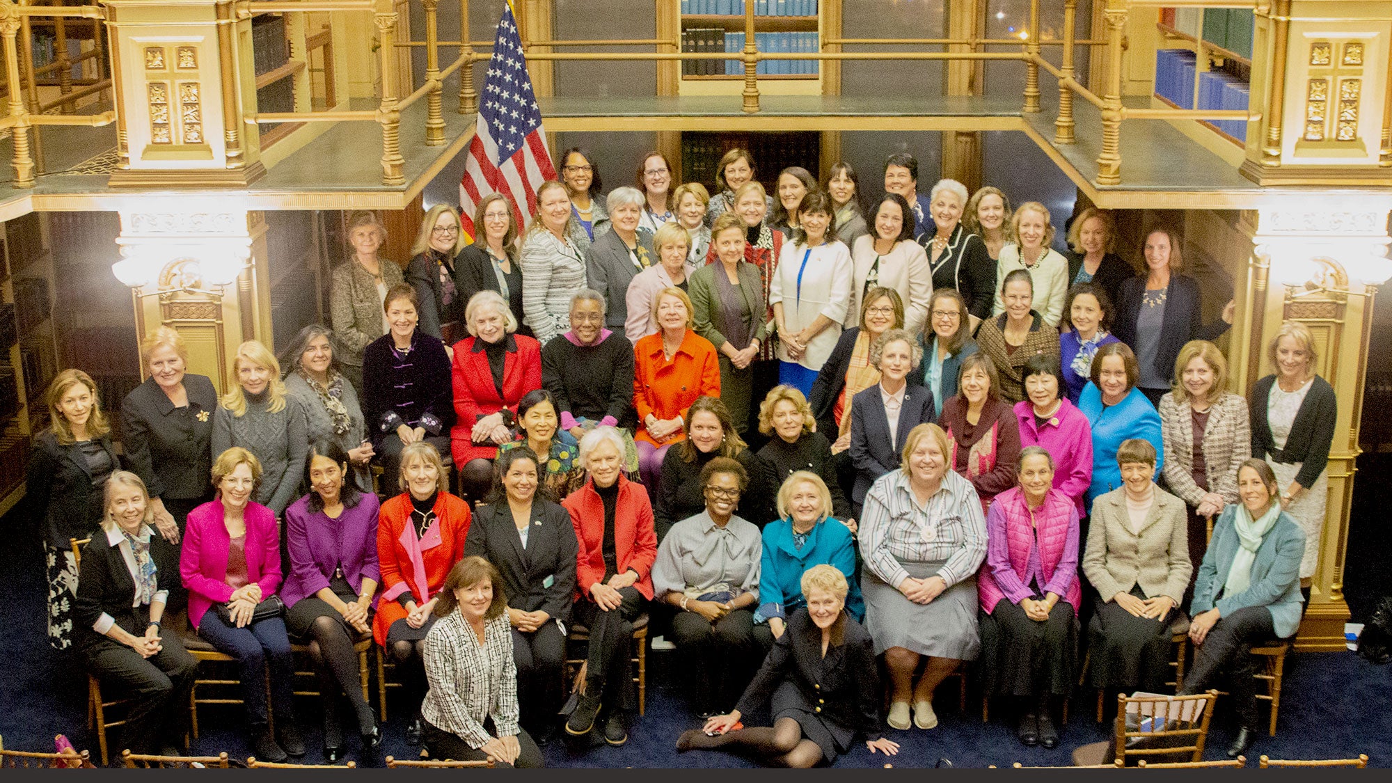 A group of about 60 women sit and stand for a photo together in Riggs Library.