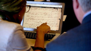 A woman and a man look at historical documents on a latop screen.