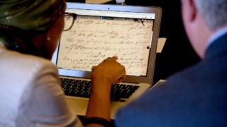 A woman and a man look at historical documents on a latop screen.