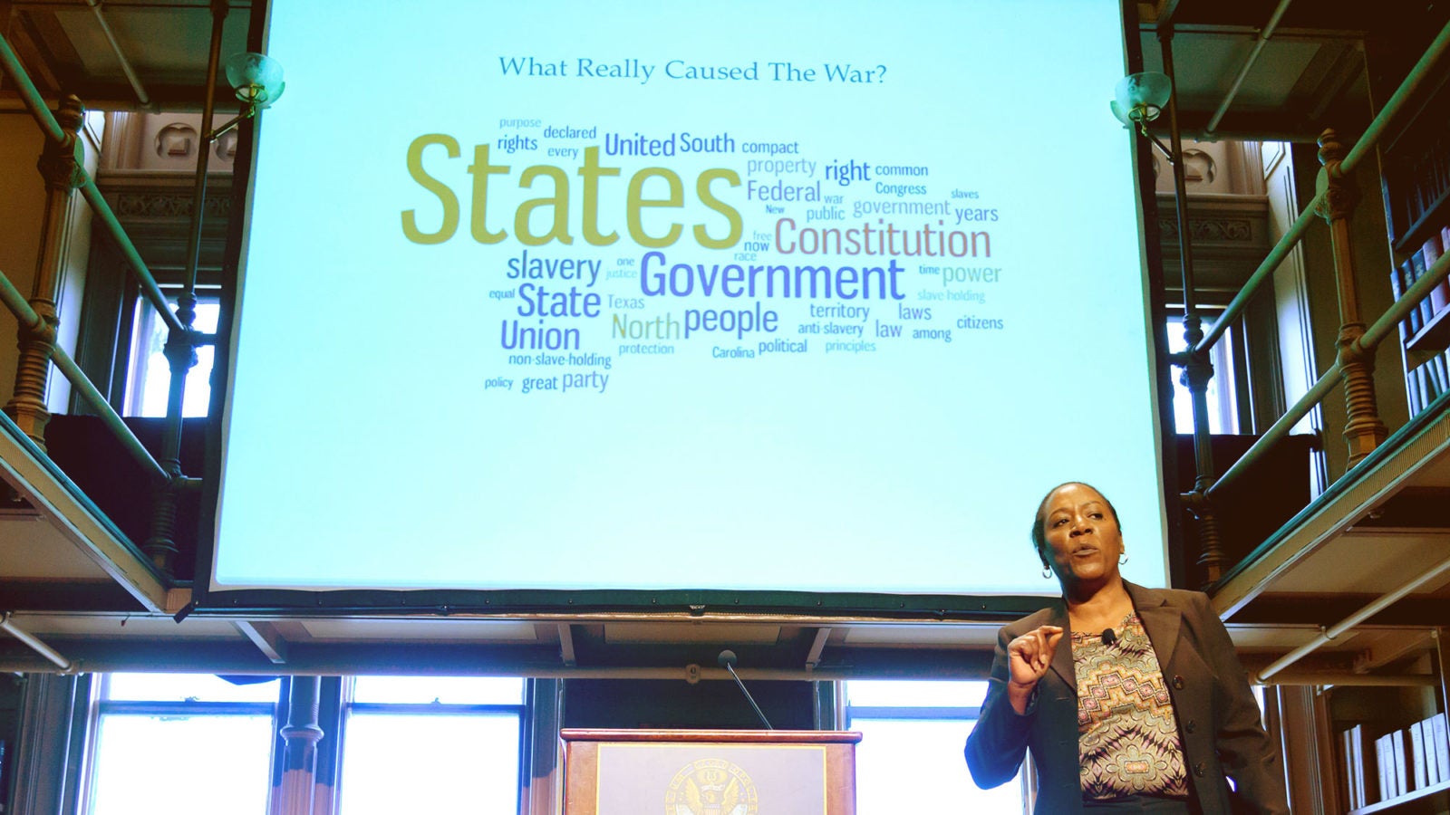 Christy Coleman stands on stage in Riggs Library with a huge screen projecting her slide presentation.