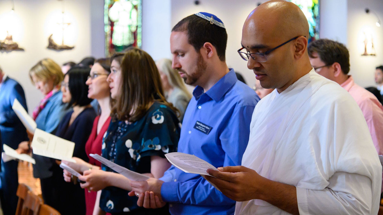 Rows men and women stand in the chapel looking at their programs and singing.