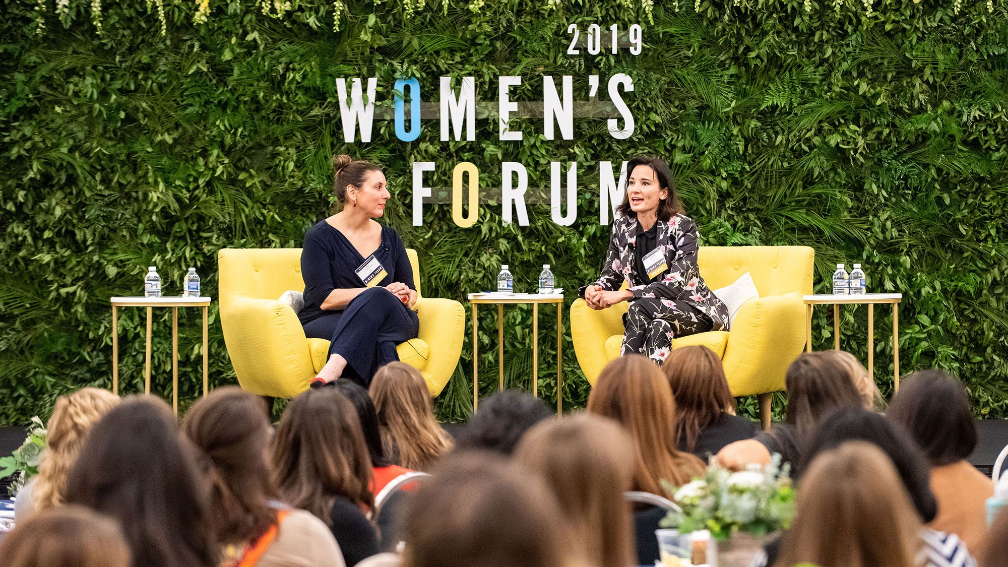 Lulu Garcia-Navarro and Alison Becker sit down on stage and talk with 2019 Women&#039;s Forum signage in the background.