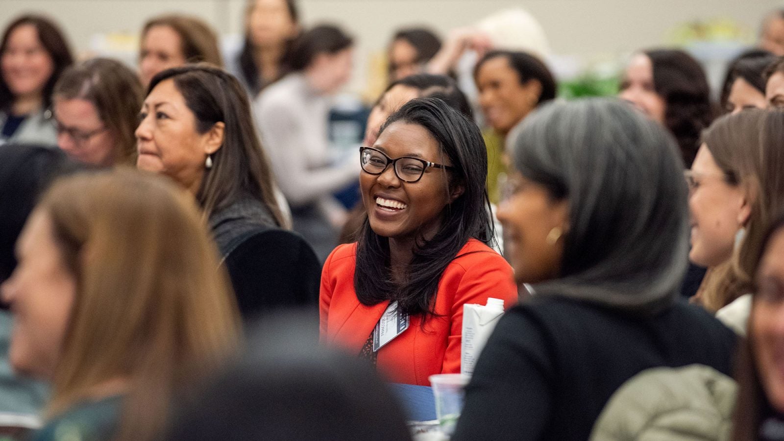 A woman smiles looking forward at the stage while surrounded by women sitting at her table.