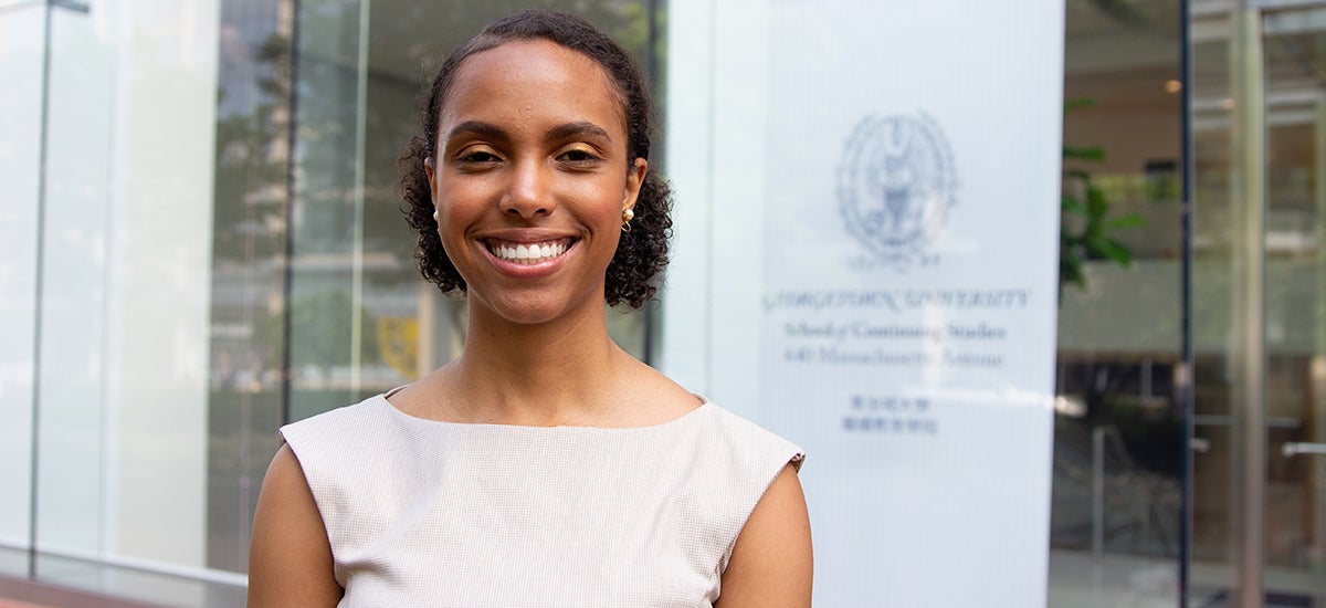 Elizabeth Thomas smile while standing with the School of Continuing Studies entrance in the background.