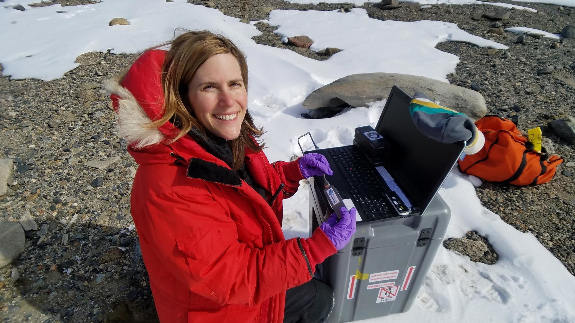 Sarah Johnson collects samples while sitting on a snow-covered ground in Antarctica.