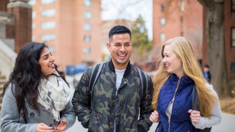 Three graduate students walk in front of a campus building.