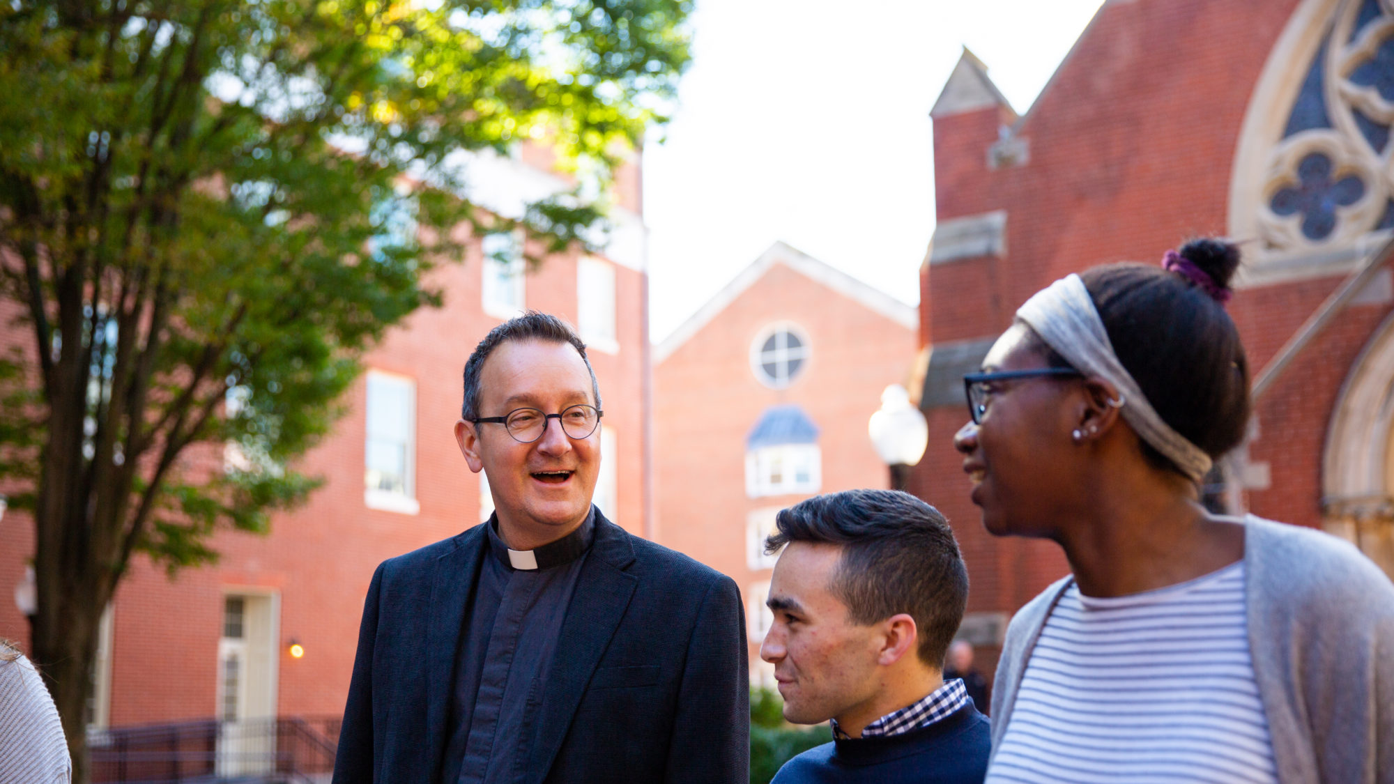 Two students talk with Fr. Bosco in Dahlgren Quad.