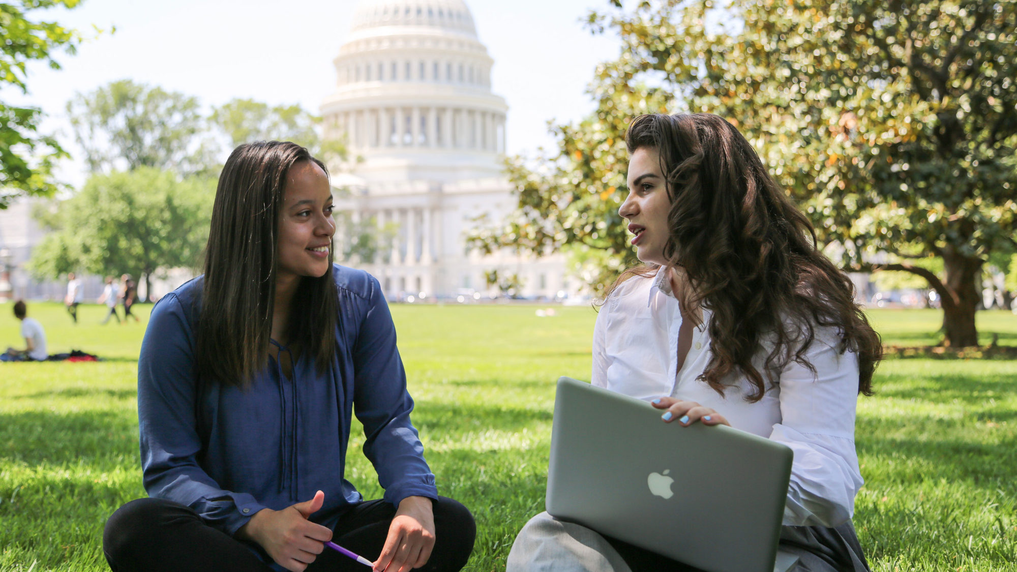 Two students work on laptops next to the Capitol Building.