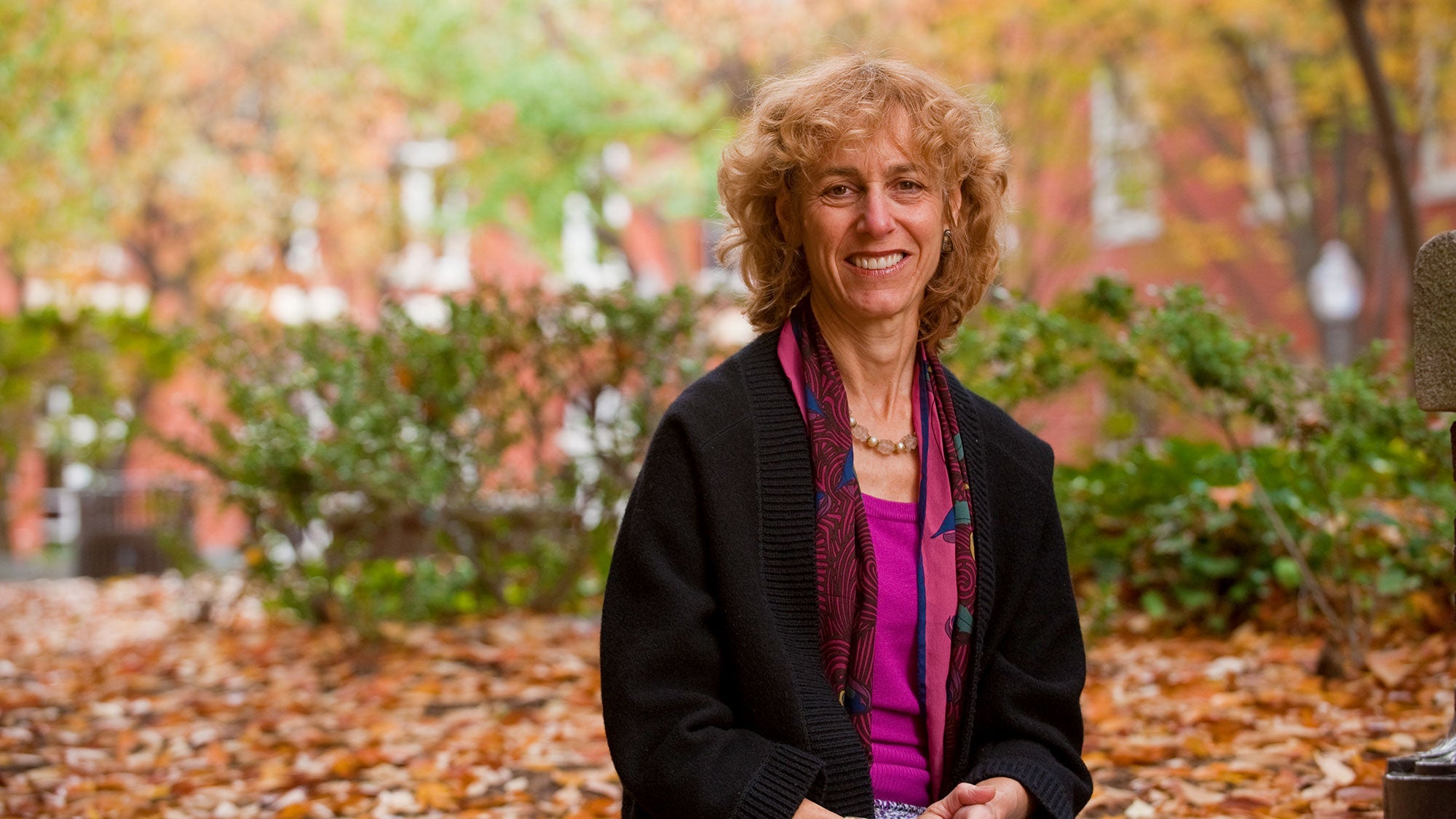 Nancy Sherman sits outside around colorful leaves on teh ground with Dahlgren Chapel in the background.