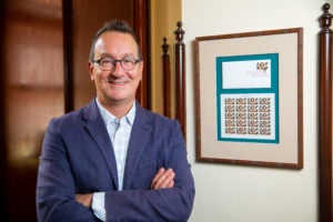 Mark Bosco stands with arms folded next to frame with Flannery O'Connor postage stamp