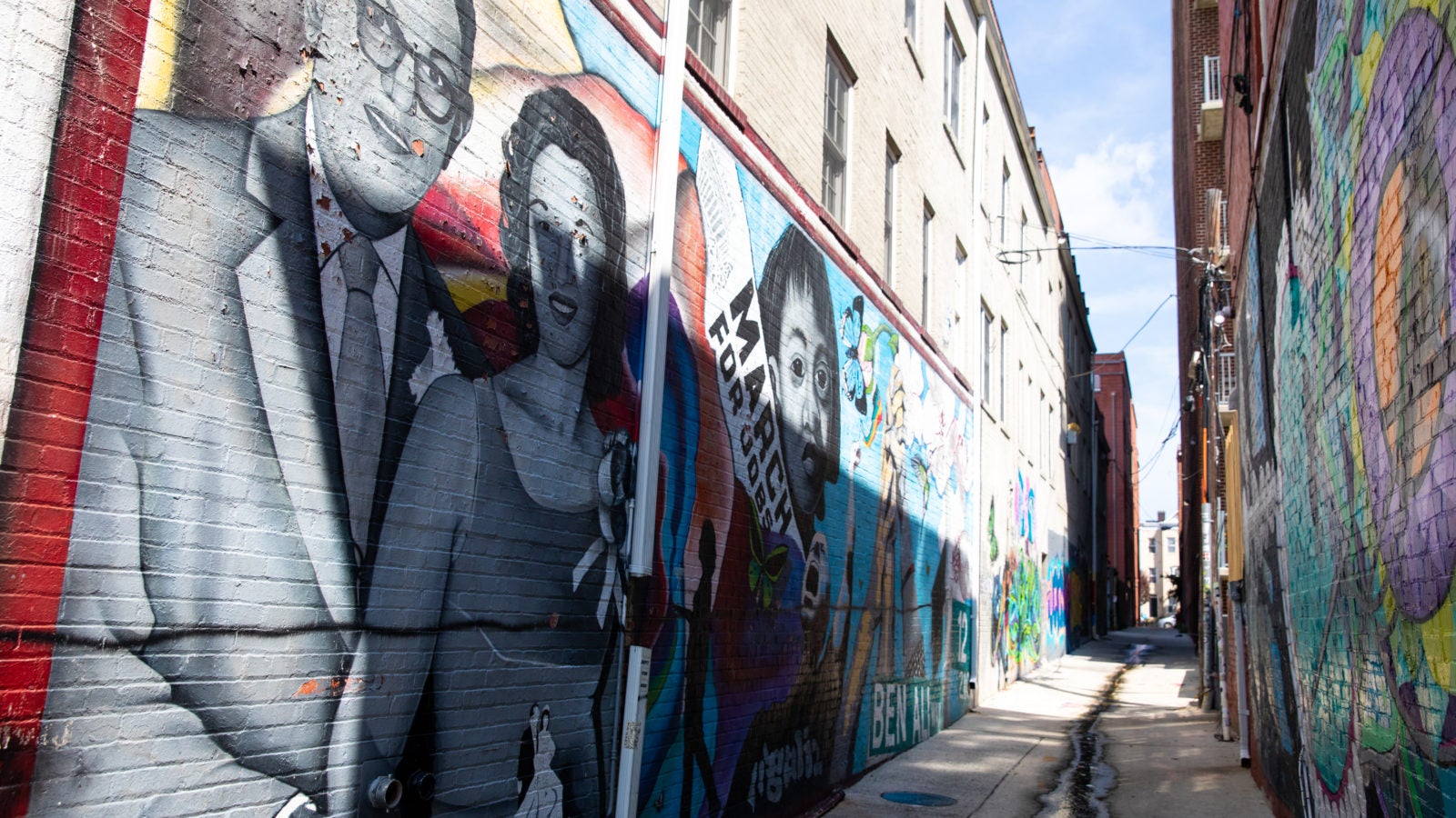 Sunlight shines down on an alley way covered in graffiti art.