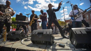 Musicians perform on stage on a sunny day underneath a blue sky dotted with clouds.