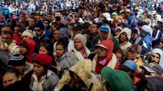 A large group of women, men and children stand gathered together on the streets in Venezuela.