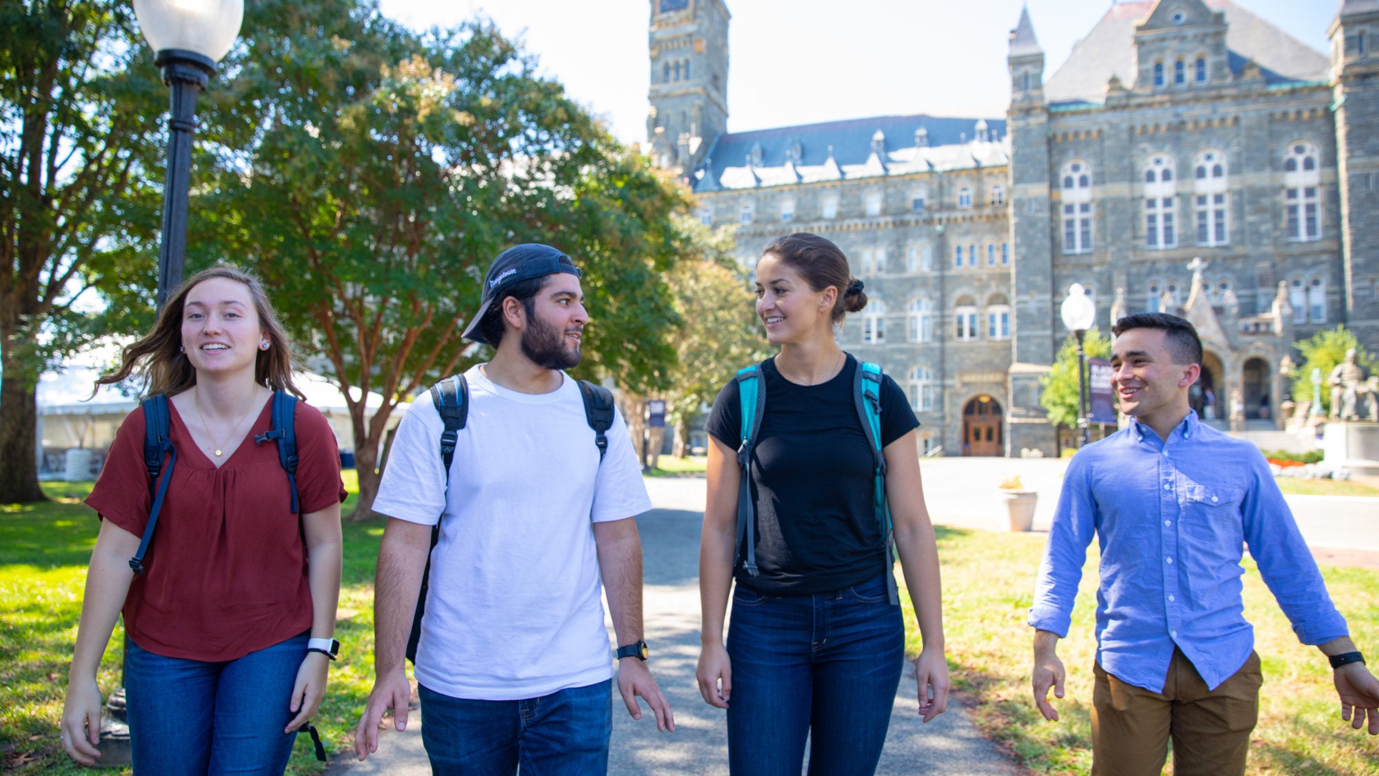 Four students with backpacks talking and walking through campus.