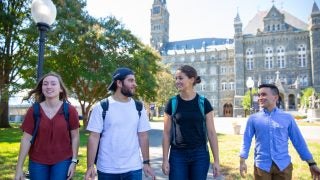 Four students with backpacks talking and walking through campus.