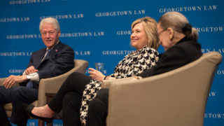 Bill Clinton and Hillary Rodham Clinton sit with Ruth Bader Ginsburg on stage with Georgetown Law signage in the background.